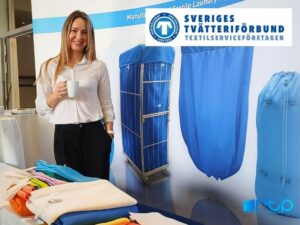 Przedstawicielka firmy RTP Radom prezentuje ofertę tekstyliów przemysłowych, w tym worki i wózki transportowe, na tle logo Sveriges Tvätteriförbund.